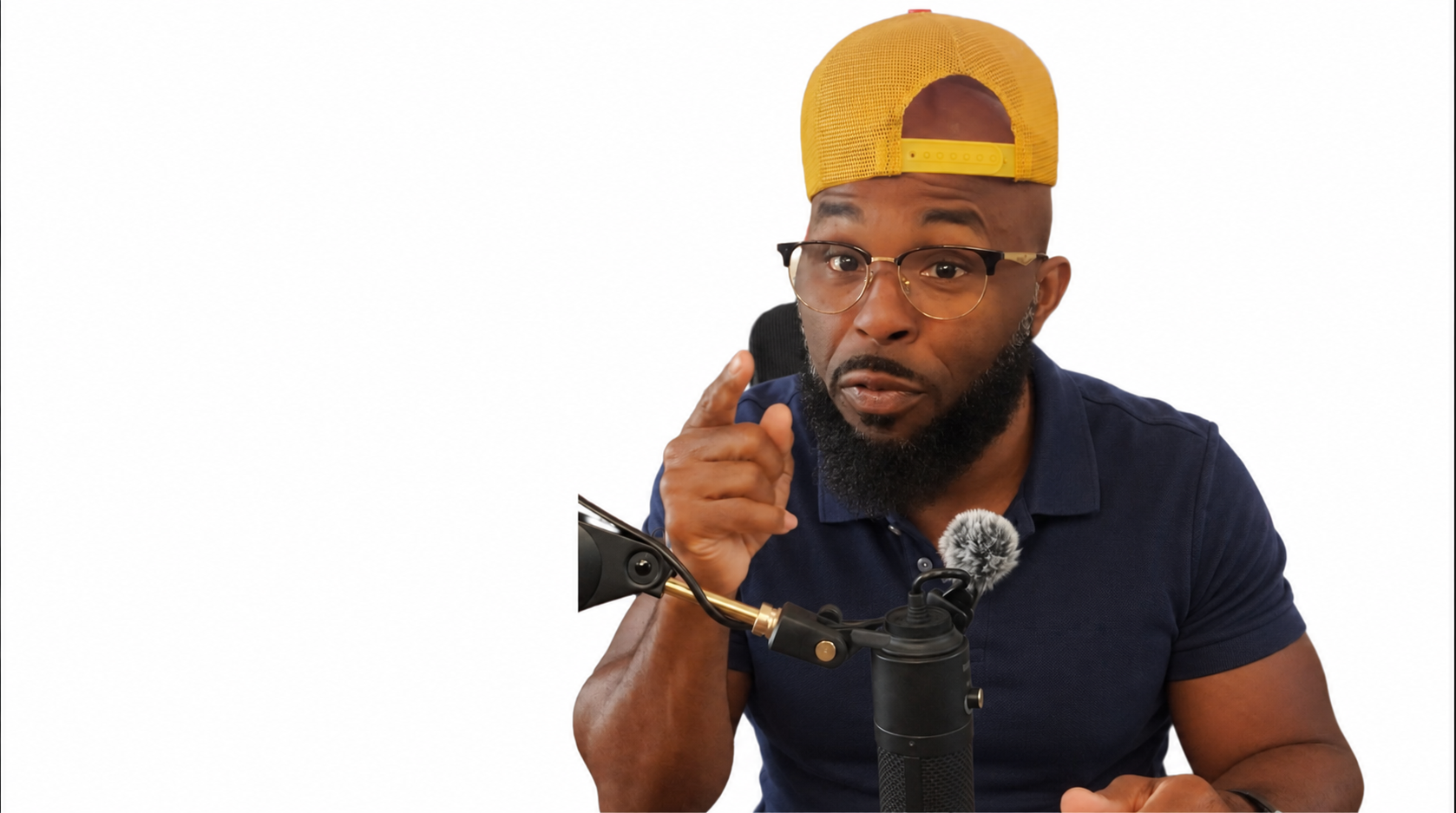 Mitch wearing a navy polo, glasses and a yellow cap at his microphone
